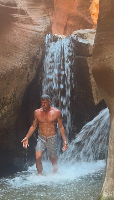 Brandon Burke moving through cascading water in a red-rock canyon